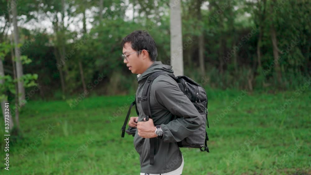 A young man carries a backpack and travels in the forest. The young man felt refreshed, surprised, and relaxed amidst the rich nature. Look at the clock, look around and continue happily hiking A young man carries a backpack and travels in the forest. The young man felt refreshed, surprised, and relaxed amidst the rich nature. Look at the clock, look around and continue happily hiking