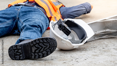 Accident and injury on a construction site. Safety first concept. Male worker lying down unconscious on the floor with safety helmet after falling from ladder. Fainting from exhaustion or heat stroke