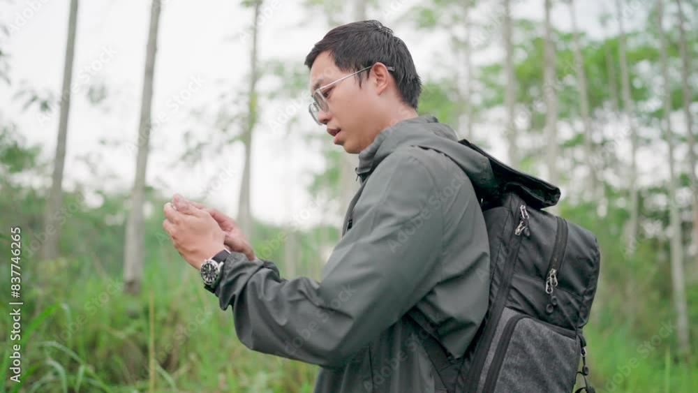A man looks at a map on a smartphone and looks at the time on a watch. Male hiker wearing hiking gear and backpack exploring the trail A man looks at a map on a smartphone and looks at the time on a watch. Male hiker wearing hiking gear and backpack exploring the trail