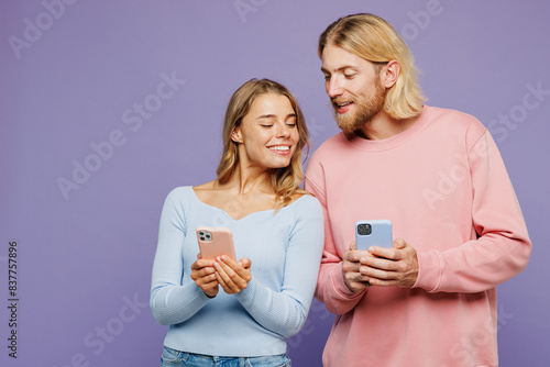 Young happy couple two friends family man woman wear pink blue casual clothes together hold in hand use looking at mobile cell phone isolated on pastel plain light purple background studio portrait. photo