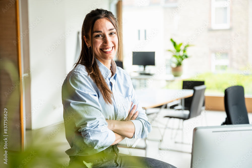 Happy young businesswoman with arms crossed sitting at office Happy young businesswoman with arms crossed sitting at office