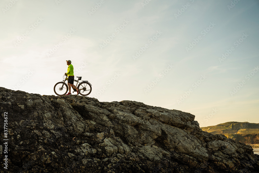 Man walking with bicycle on rock at sunset Man walking with bicycle on rock at sunset