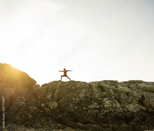 Man practicing worrier pose on rock under sky at sunset