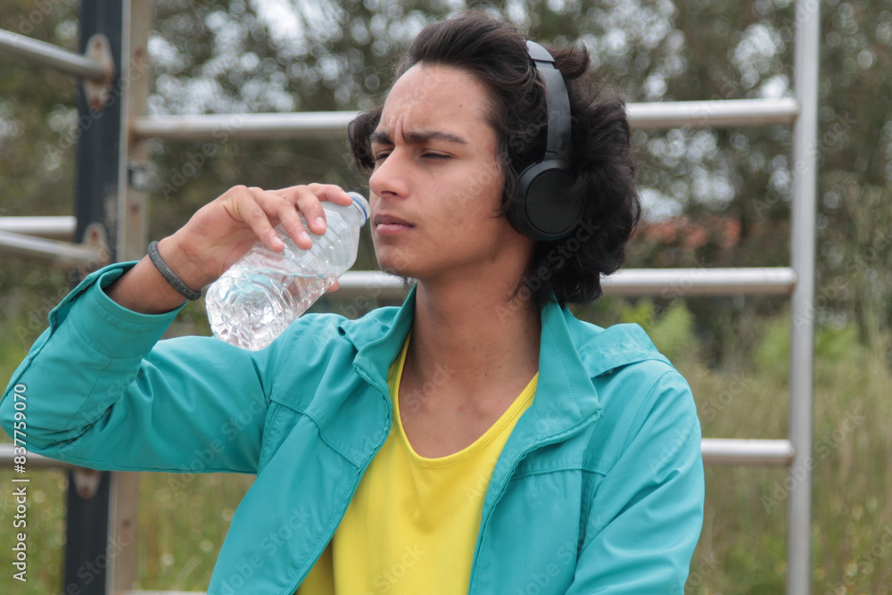 young man with headphones drinking after doing sports outdoors young man with headphones drinking after doing sports outdoors