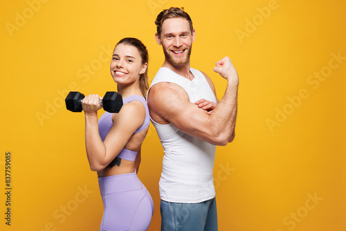 Fototapeta Naklejka Na Ścianę i Meble -  Side view young strong fitness trainer instructor sporty two man woman wearing blue clothes spend time in home gym hold in hand dumbbells isolated on plain yellow background Workout sport fit concept