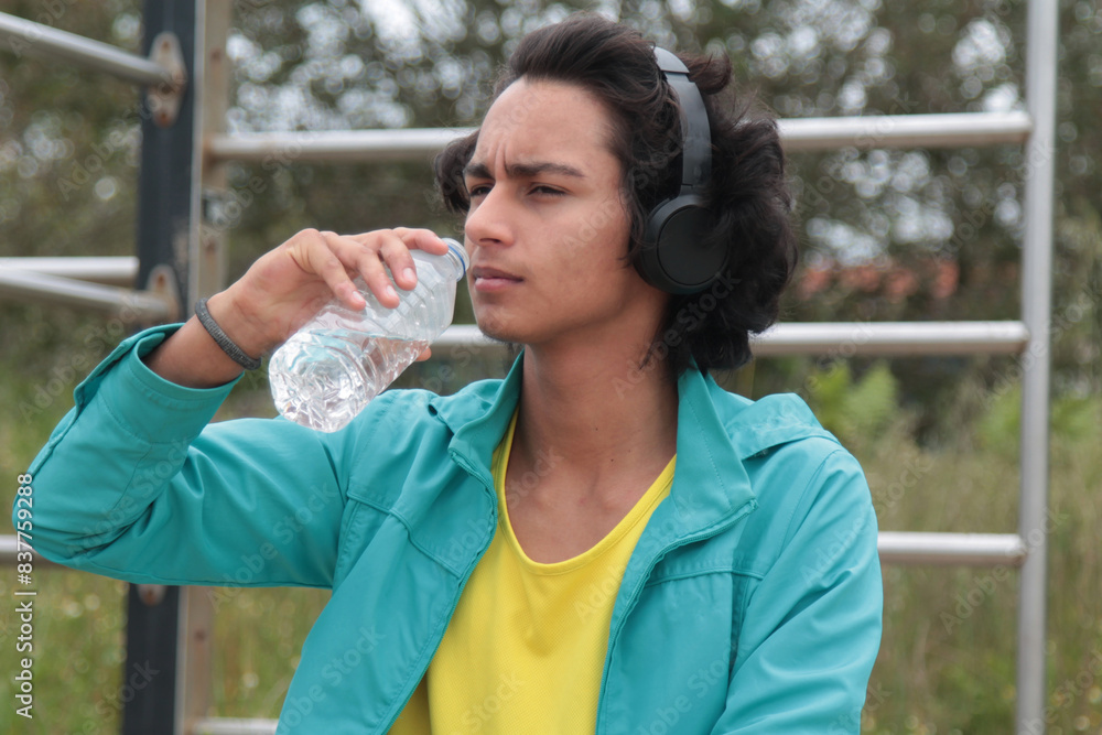 young man with headphones drinking after doing sports outdoors young man with headphones drinking after doing sports outdoors