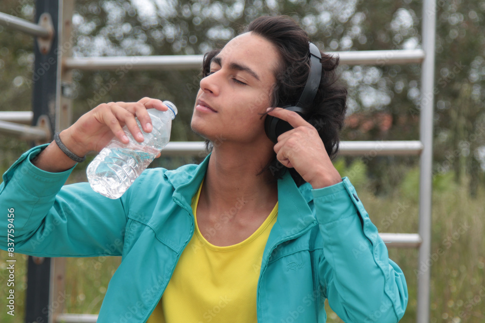 young man with headphones drinking after doing sports outdoors young man with headphones drinking after doing sports outdoors