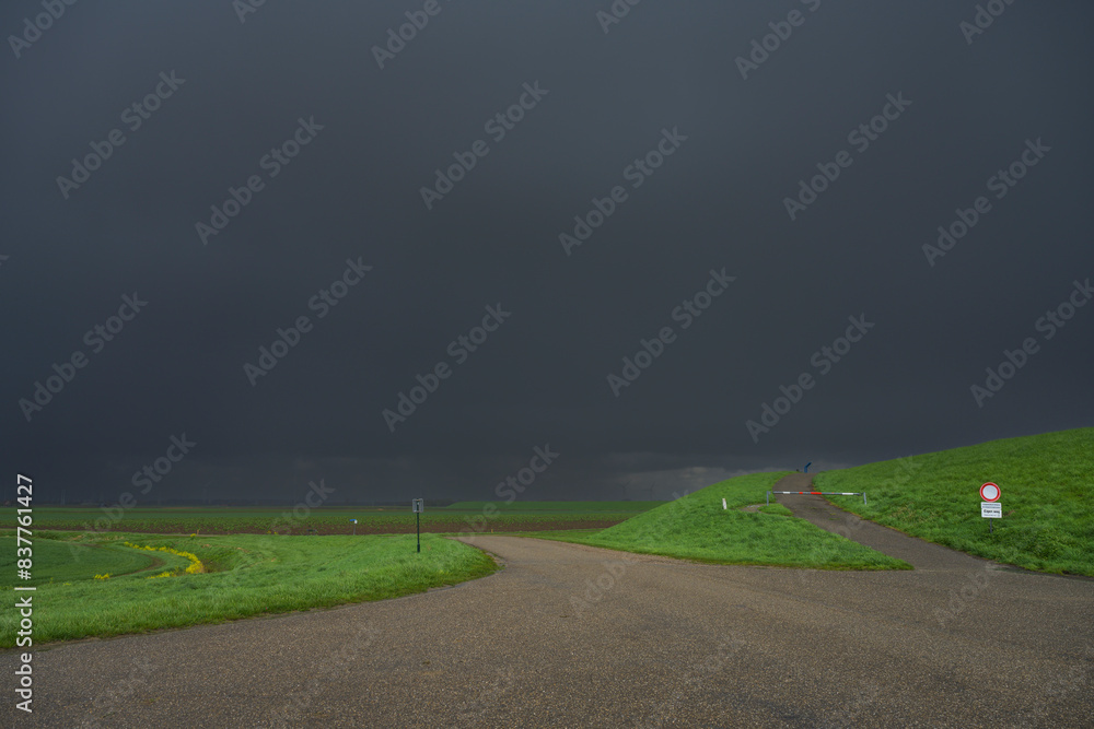 Netherlands, Zeeland, Dark rain clouds over asphalt road and green levee Netherlands, Zeeland, Dark rain clouds over asphalt road and green levee