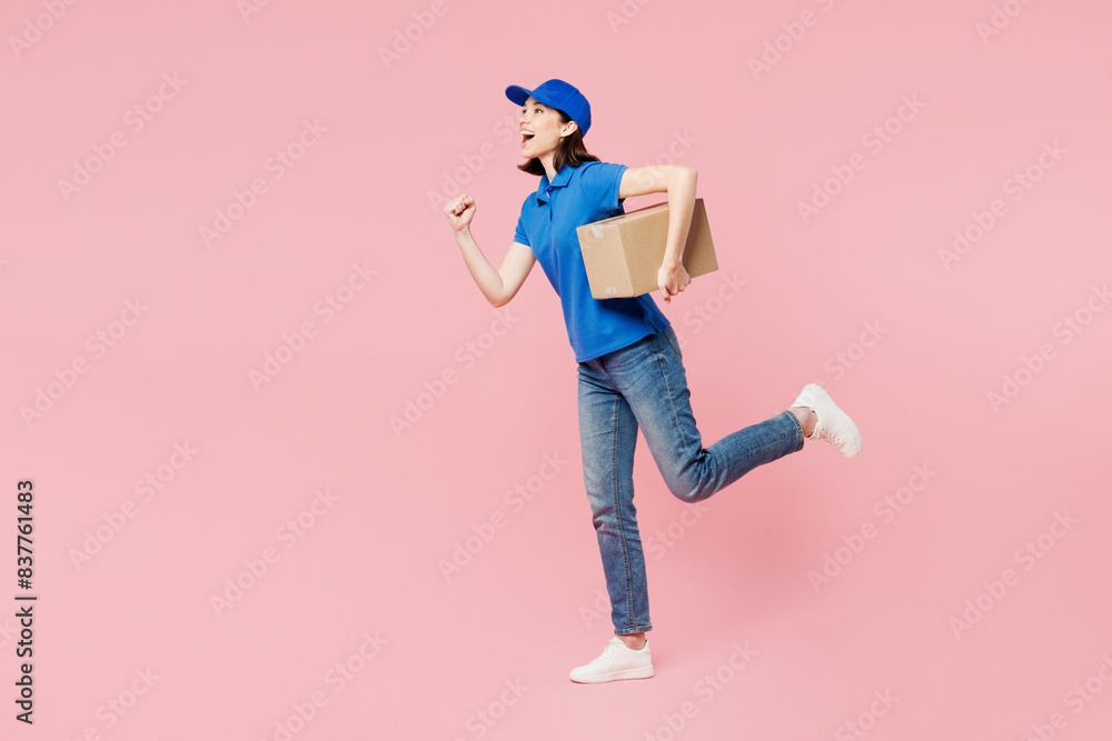 Full body side view delivery girl employee woman wear blue cap t-shirt uniform workwear work as dealer courier hold give cardboard box run hurry up isolated on plain pink background Service concept. Full body side view delivery girl employee woman wear blue cap t-shirt uniform workwear work as dealer courier hold give cardboard box run hurry up isolated on plain pink background Service concept.