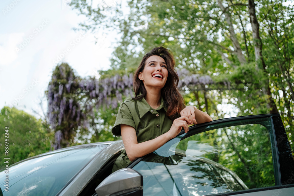 Happy woman leaning on car door in front of tree Happy woman leaning on car door in front of tree