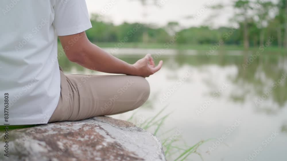 A healthy young man meditates on a large rock by the water. He sat cross-legged amidst beautiful nature A healthy young man meditates on a large rock by the water. He sat cross-legged amidst beautiful nature