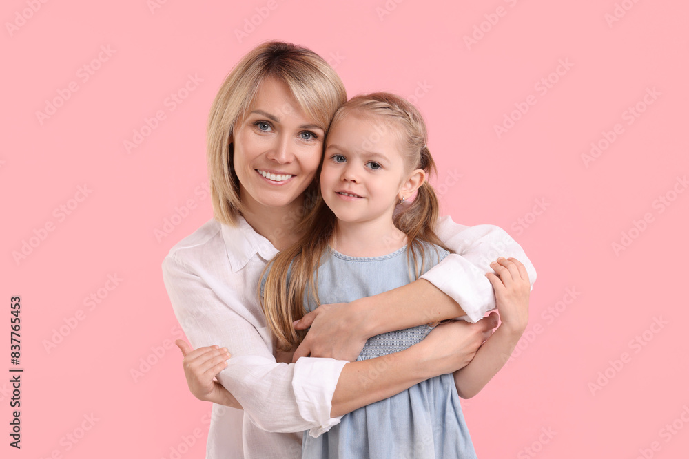 Mother hugging her happy daughter on pink background Mother hugging her happy daughter on pink background