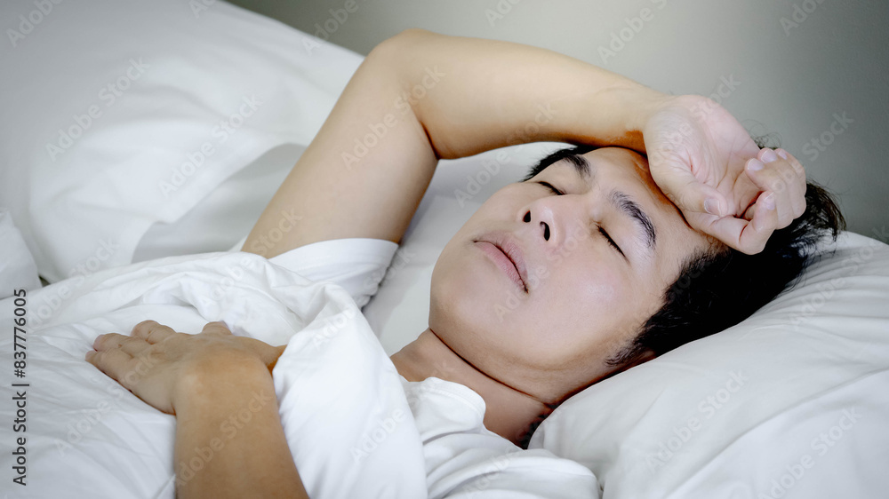Depressed mature Asian man touching his forehead suffering from insomnia and headache while lying on the bed. Feeling worried and stressed before bedtime. Mental health disorder concept Depressed mature Asian man touching his forehead suffering from insomnia and headache while lying on the bed. Feeling worried and stressed before bedtime. Mental health disorder concept