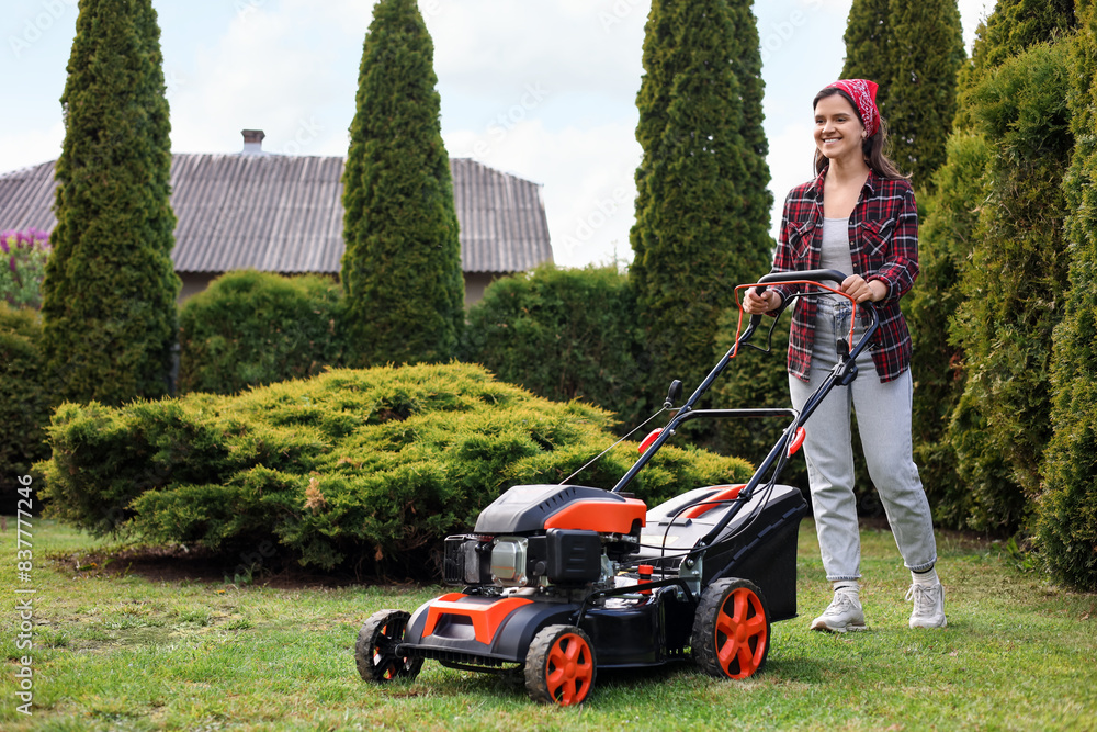 Smiling woman cutting green grass with lawn mower in garden Smiling woman cutting green grass with lawn mower in garden