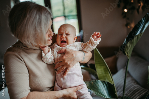 Grandmother holding crying baby girl in arms, calming her down, soothing her. Strong bond between grandparent and grandchild. photo