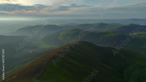 Ancient rounded glaciated forested mountains and fells misting into lowlands at golden hour. From Grisedale Pike, Lake District, Cumbria, England, UK photo