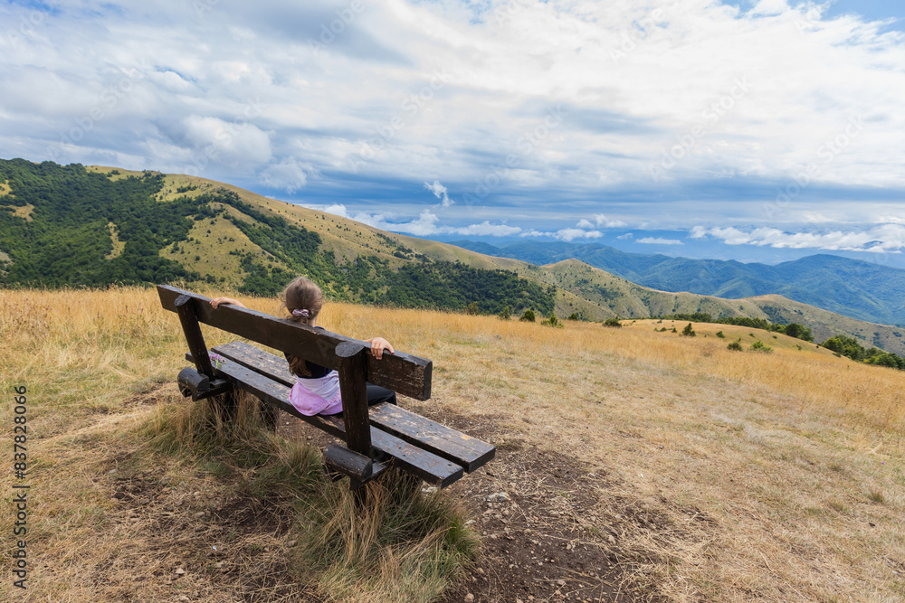 Child sitting on bench with amazing view on mountain landscape on summer day.