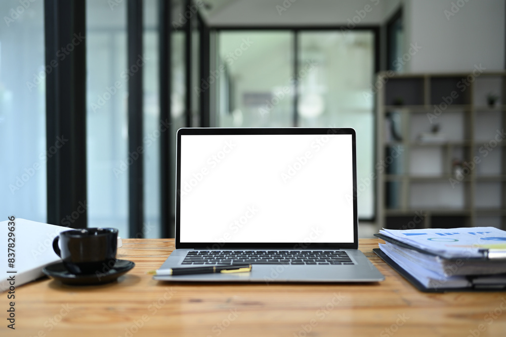 Front view laptop with empty display, documents and coffee cup on wooden office desk Front view laptop with empty display, documents and coffee cup on wooden office desk