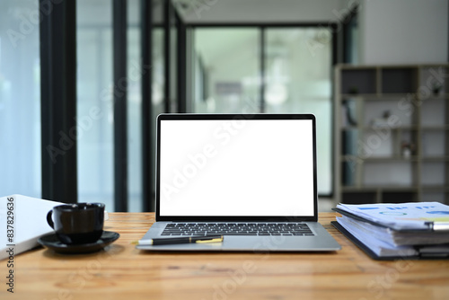 Front view laptop with empty display, documents and coffee cup on wooden office desk