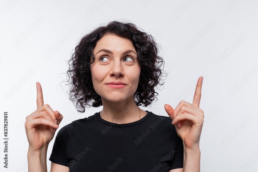 Smart brunette with curly hairstyle dressed in a black T-shirt holds her index finger up Smart brunette with curly hairstyle dressed in a black T-shirt holds her index finger up