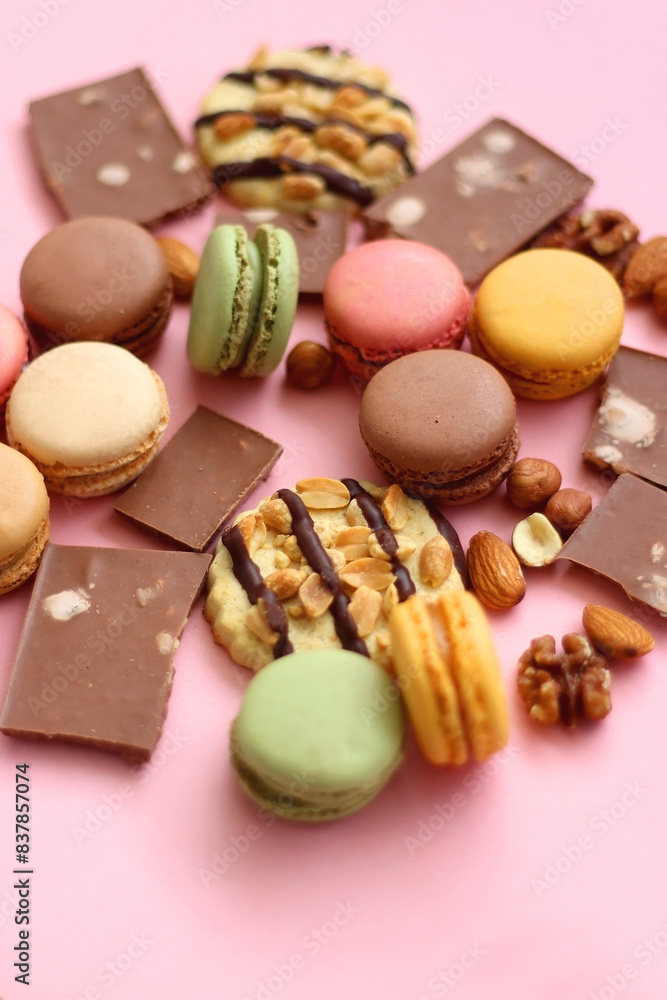 Pastel macarons, almond chocolate, peanut butter cookies and various nuts on bright pink background. Selective focus. Pastel macarons, almond chocolate, peanut butter cookies and various nuts on bright pink background. Selective focus.