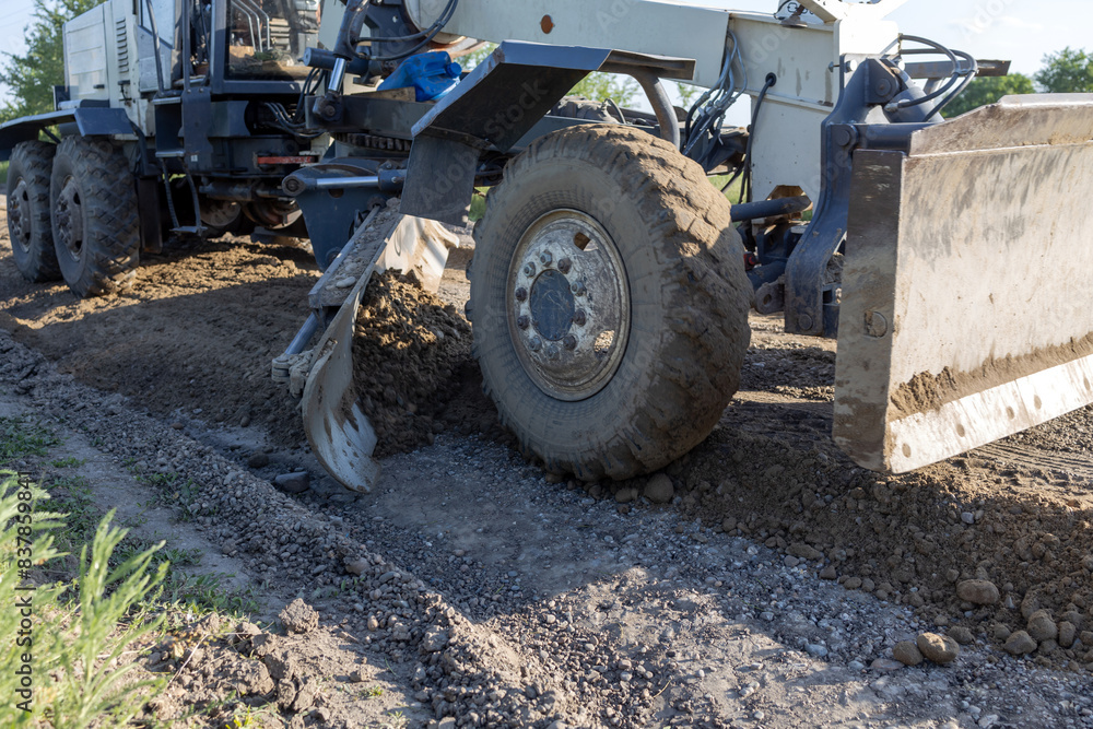 A grader levels gravel during road construction. A grader levels gravel during road construction.