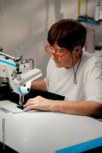 in a sewing workshop on a machine the old seamstress master makes cut on a black fabric