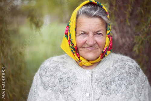 Close up portrait of a senior woman wearing a yellow headscarf in a garden. 