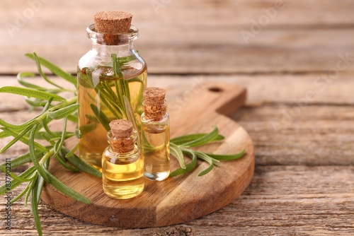 Aromatic essential oils in bottles and rosemary on wooden table  closeup. Space for text