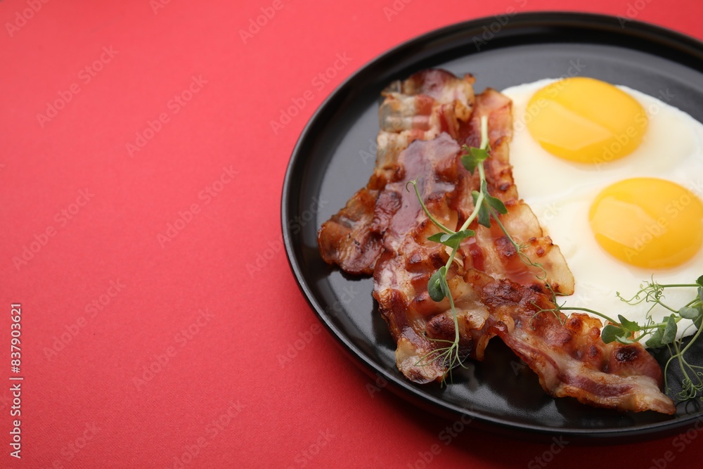 Fried eggs, bacon and microgreens on red background, space for text Fried eggs, bacon and microgreens on red background, space for text
