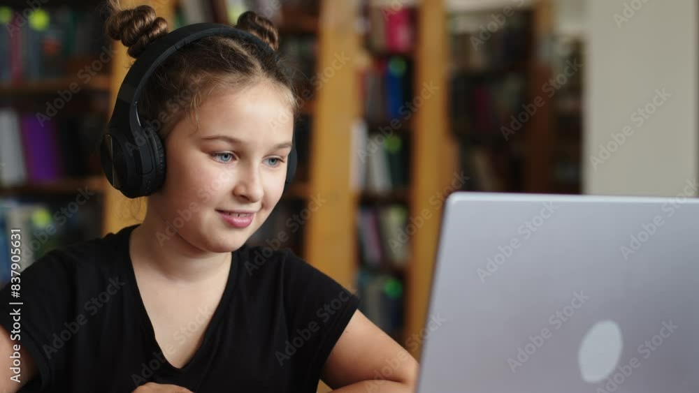 Focused student writes notes, uses laptop in public library. A student watches a webinar, an online lesson. Online learning, school and development concept. Focused student writes notes, uses laptop in public library. A student watches a webinar, an online lesson. Online learning, school and development concept.