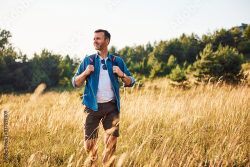 Bild auf Leinwand Mid adult man walking alone with backpack in countryside during summer weekend t