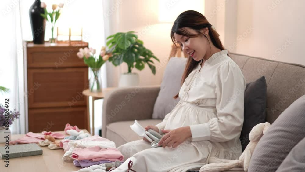 An Asian pregnant woman is playing music through headphones for her unborn baby while sitting on the sofa at home An Asian pregnant woman is playing music through headphones for her unborn baby while sitting on the sofa at home