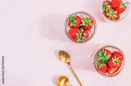 Healthy breakfast of overnight oats with yogurt and fresh strawberries, served in glass jars on a vibrant pink tile table Bathed in natural light the composition creates a cheerful atmosphere Top view photo