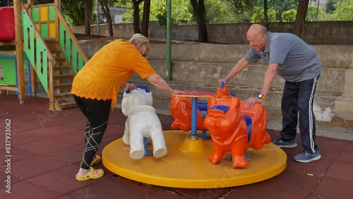 nice elderly couple playing at the children's playground, with slide, swing and rides. youth in the elderly.