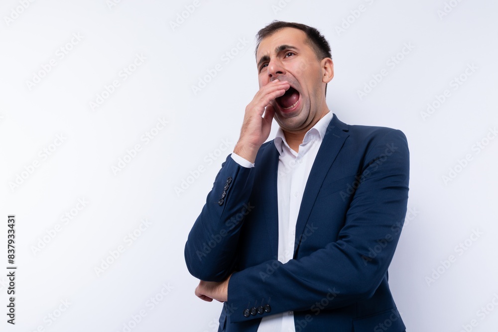 Caucasian man dressed in a blue jacket yawns from boredom on a white background Caucasian man dressed in a blue jacket yawns from boredom on a white background
