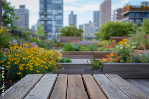 A wooden bench in the foreground with a blurred background of a rooftop garden. The background includes raised garden beds with flowers and vegetables  seating areas  and city skyline views.