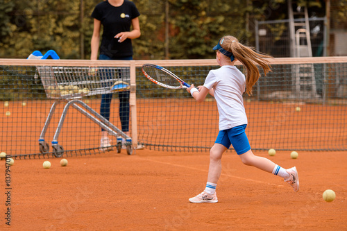 Back view of little girl actively running and playing tennis with coach with tennis racket on the outdoor tennis court photo