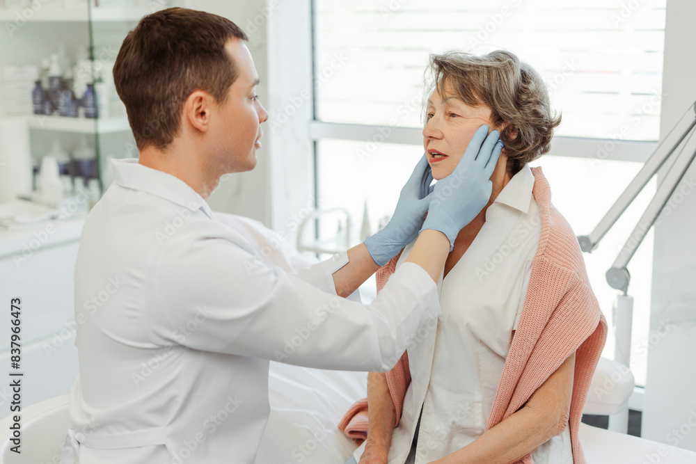 Fototapeta premium Attractive cosmetologist, man touching face of senior patient, lifting, tightening, rejuvenation