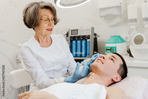 Smiling senior mature woman doing cosmetic procedures in modern clinic  removing wrinkles near eyes
