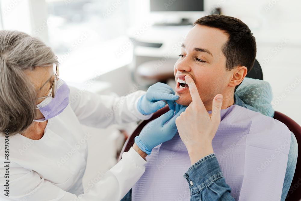 Attractive young man, patient having toothache, showing teeth to professional, senior doctor Attractive young man, patient having toothache, showing teeth to professional, senior doctor
