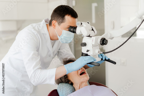 Professional dentist doctor, man treating teeth using dental microscope, checking senior woman