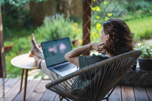 Obraz na płótnie Young adult Caucasian woman sitting on cottage terrace using laptop in summertime, online work w salonie