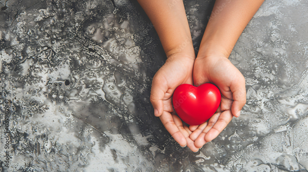 Adult and child hands holding a red heart on an aqua background symbolize heart health, donation, corporate social responsibility, World Heart Day, World Health Day, and Family Day.