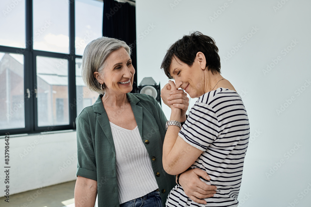 Naklejka premium Two women, middle-aged, stand by a window, sharing a candid moment of companionship and collaboration in a modern studio.