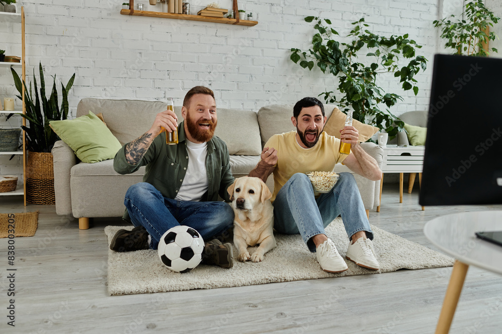 Two men, with beards, sit on rug with Labrador dog, watching sport match in living room. Two men, with beards, sit on rug with Labrador dog, watching sport match in living room.