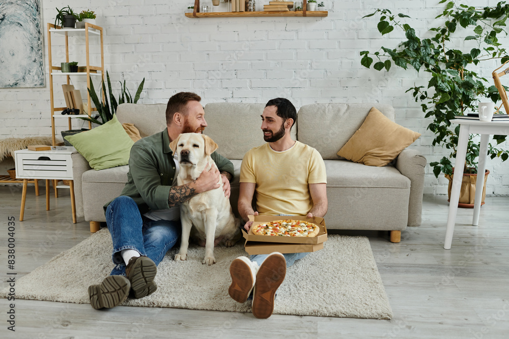 Two men with beards relax on a couch with a box of pizza, sharing a slice while a friendly Labrador looks on. Two men with beards relax on a couch with a box of pizza, sharing a slice while a friendly Labrador looks on.