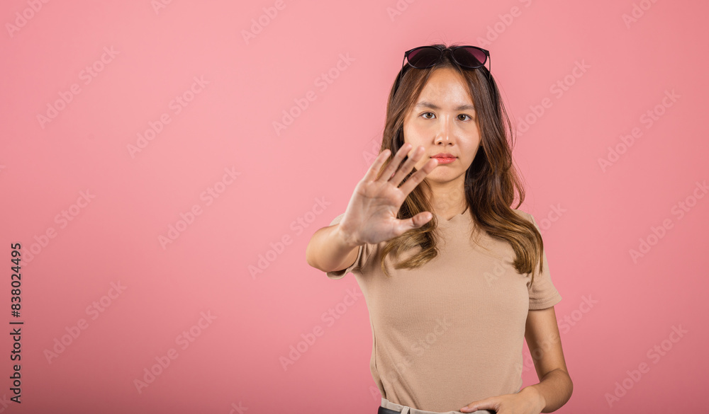 Asian beautiful woman itching her outstretched hand showing stop gesture front face on pink background with copy space, female doing show stop sign with palm of hand Asian beautiful woman itching her outstretched hand showing stop gesture front face on pink background with copy space, female doing show stop sign with palm of hand