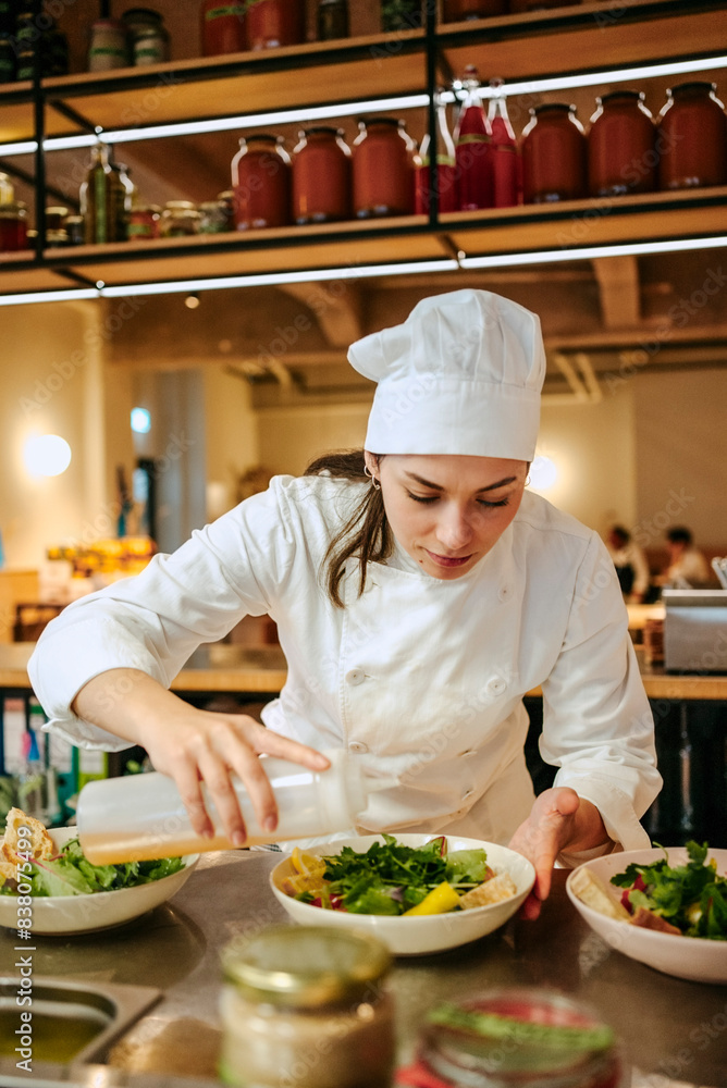Young female chef pouring oil on salad in commercial kitchen Young female chef pouring oil on salad in commercial kitchen