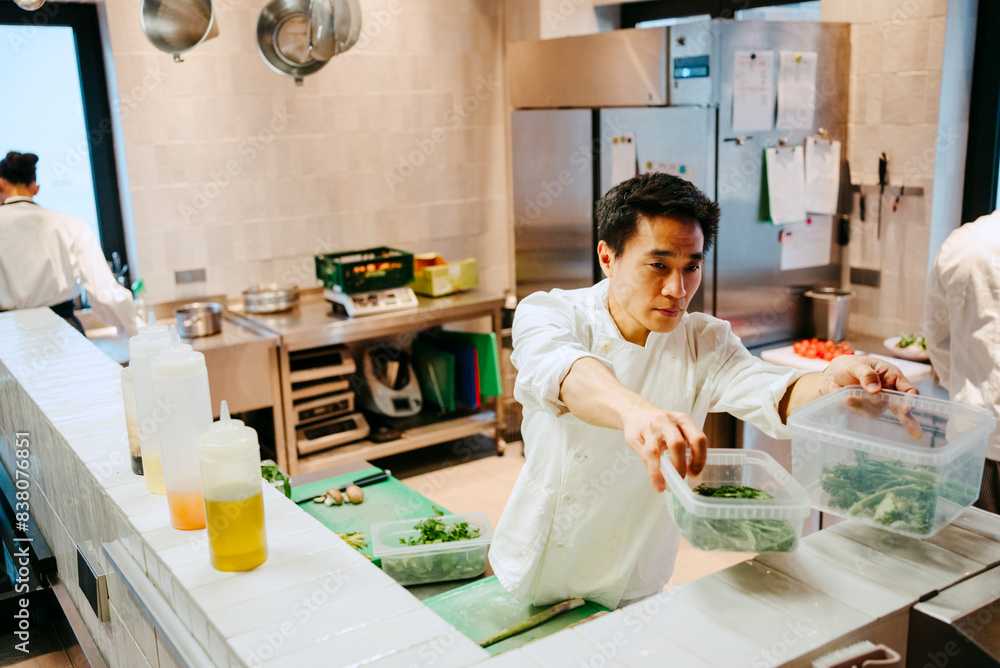 Male chef passing broccolini container while working in commercial kitchen Male chef passing broccolini container while working in commercial kitchen